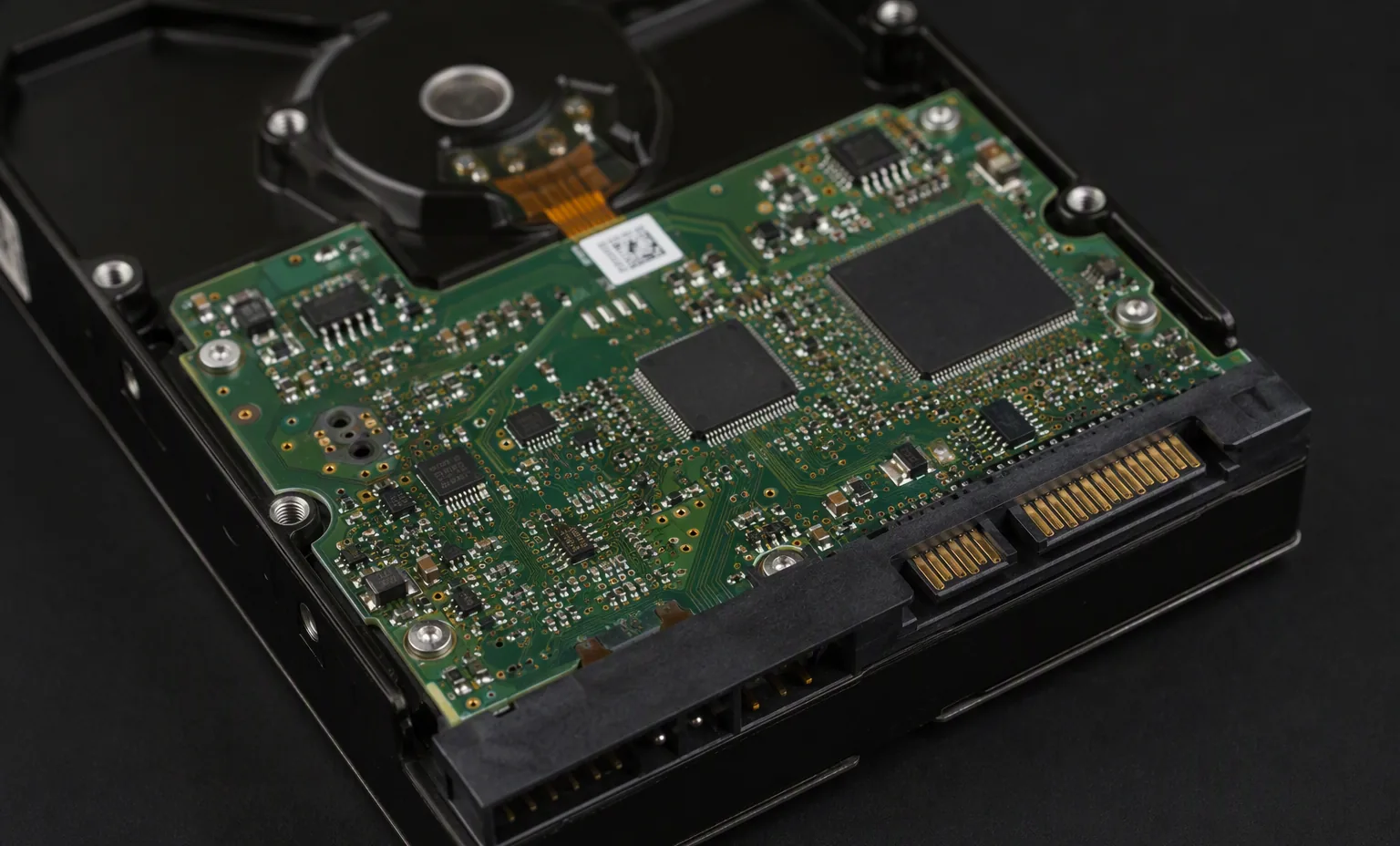 Photorealistic macro photograph of the green controller PCB underside of a real enterprise SAS hard drive, visible chips and SATA power connector, dark studio.