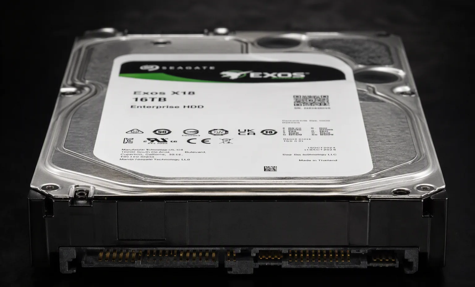 Seagate Exos X18 16TB enterprise HDD front edge view showing SATA SAS connector, dark macro studio shot.