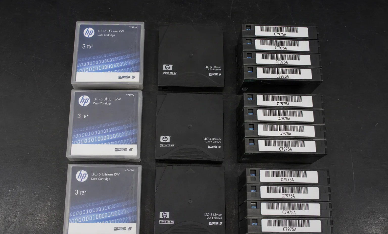 Photorealistic photograph of LTO tape cartridges with barcode labels arranged for inventory on a dark lab bench, top view.