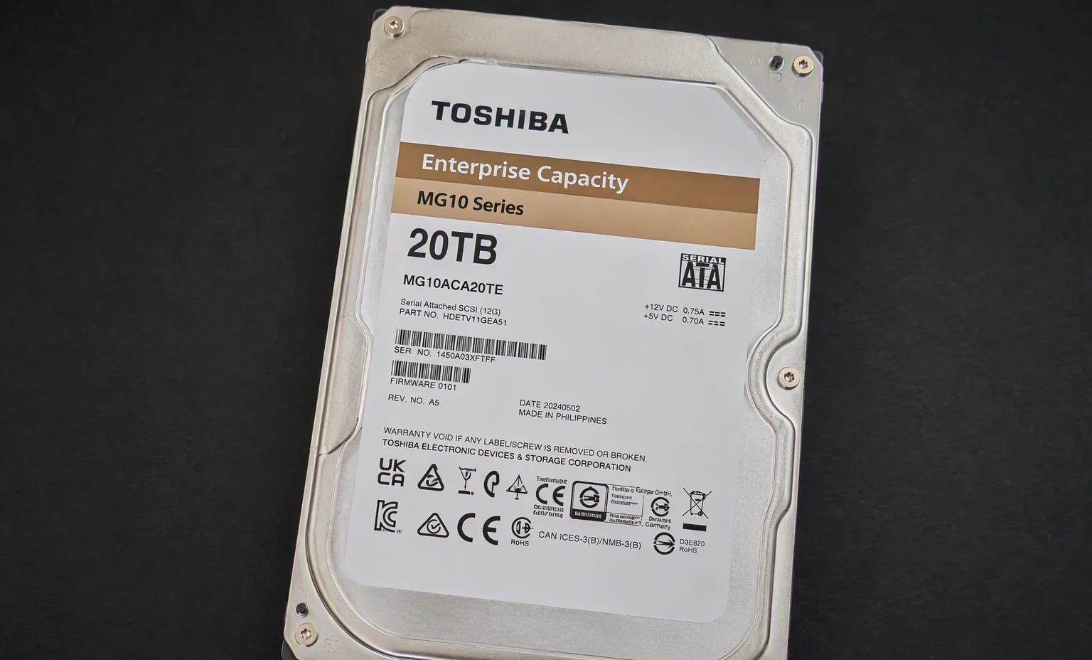 Toshiba MG10 20TB enterprise hard drive label side, on dark matte surface, macro product photography.