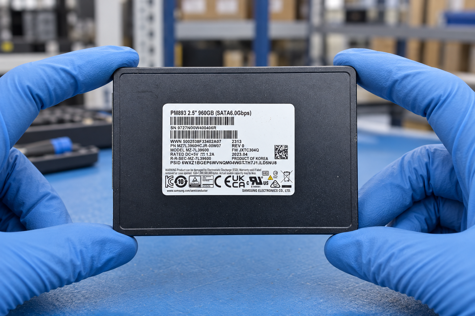 Samsung MZ7L3960HCJR-00W07 held by two blue-gloved hands above a blue electronics workbench; generated scene